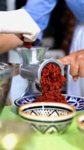A silver metal meet grinder is used to produce a puree of red chilies